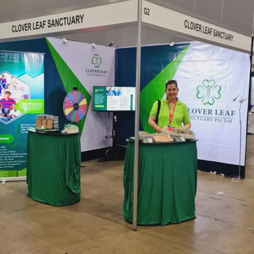 Clover Leaf Sanctuary's expo booth with overhead signage, a registered NDIS provider banner and a staff member at the table